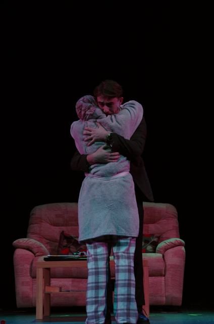 Two performers hugging beside a pink sofa