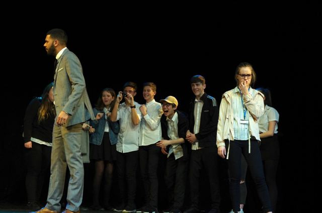 A class of pupils giggling behind a tall teacher