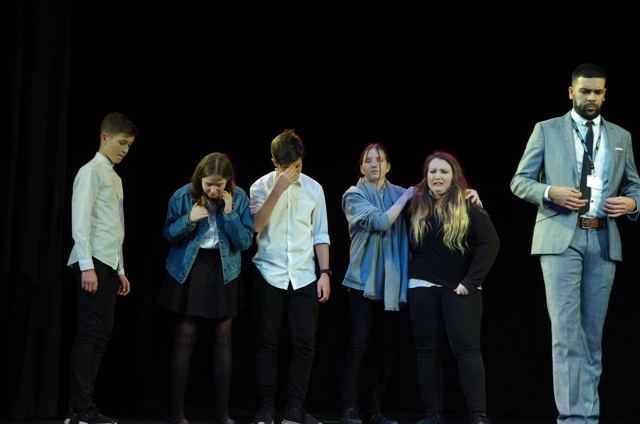 Pupils standing in a line, a teacher in a grey suit at the end