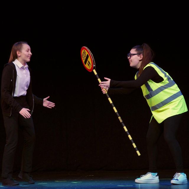 A lollipop lady in a hi-vis vest holding up her sign to a pupil