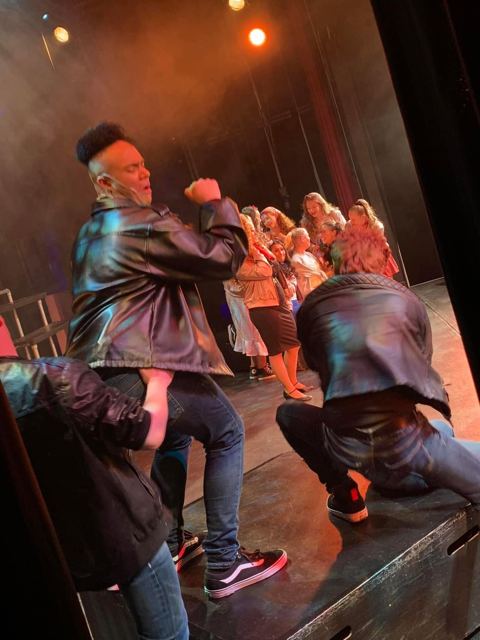 Performers in leather jackets singing and dancing in red light