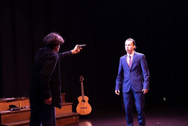 A performer pointing a gun at a young man in a blue suit