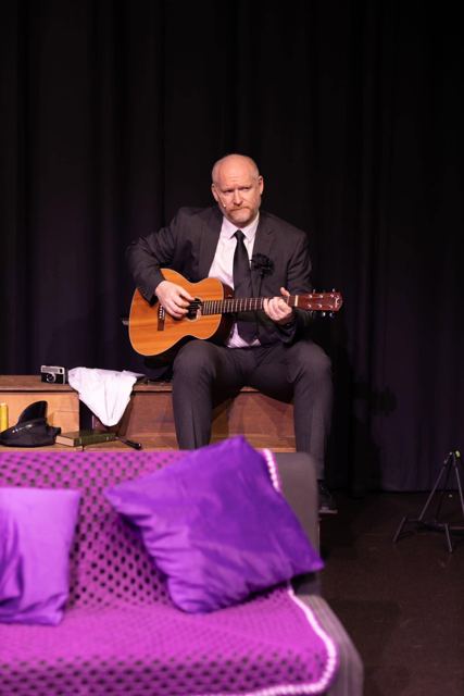 A man in a black suit playing guitar on stage