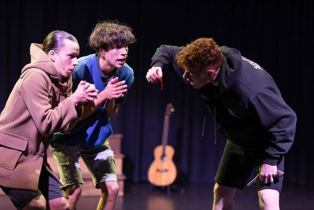 Three young performers crouching together, plotting