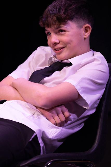 A young man in a school shirt and tie leaning back with a grin