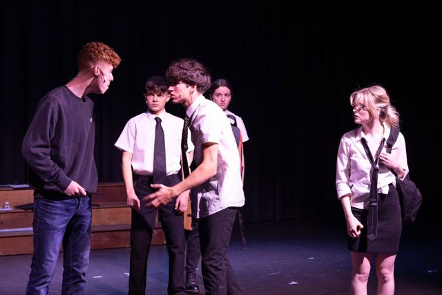Schoolboys whispering together while a girl looks on