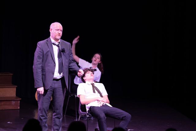A man in a suit standing over a seated young man