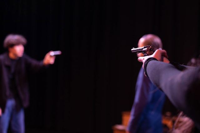 Two performers aiming guns at each other