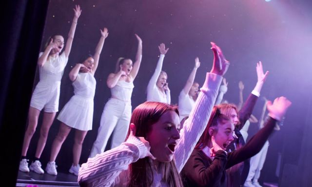 Performers in white with their arms raised, dancing