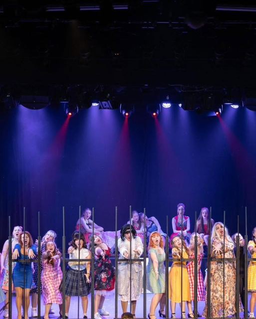 The cast lined up behind bars under blue light
