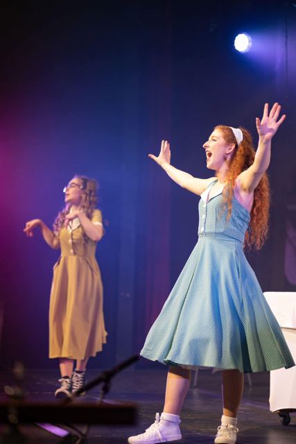 A performer in a blue dress throwing her arms out with joy