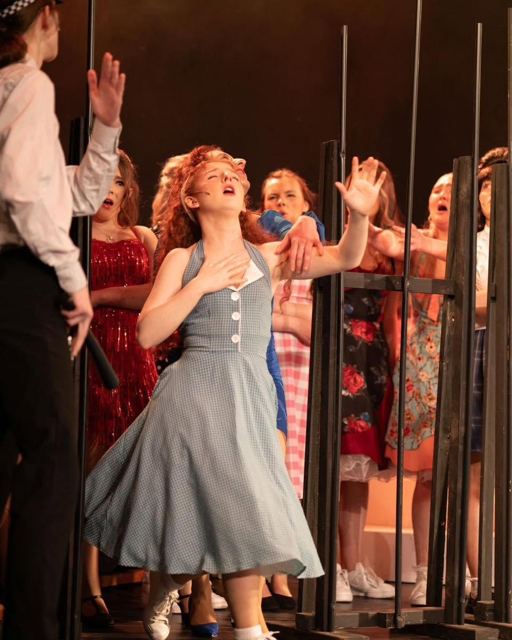 A performer in a blue dress reaching out as she sings
