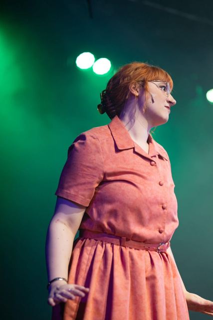 A performer in a coral dress under green light