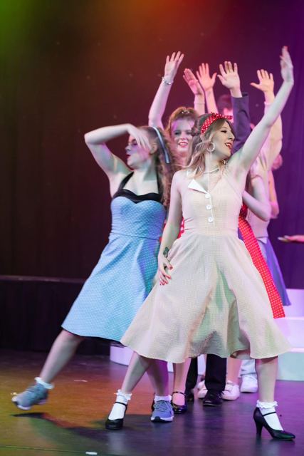 Dancers in 1960s dresses with their arms raised