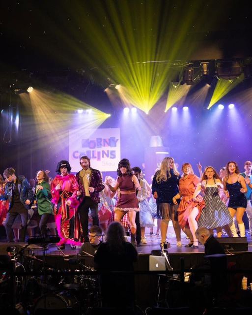 A wide view of the full company dancing under the Corny Collins Show sign