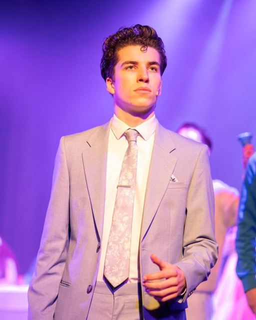 A young man in a grey suit and tie under purple light