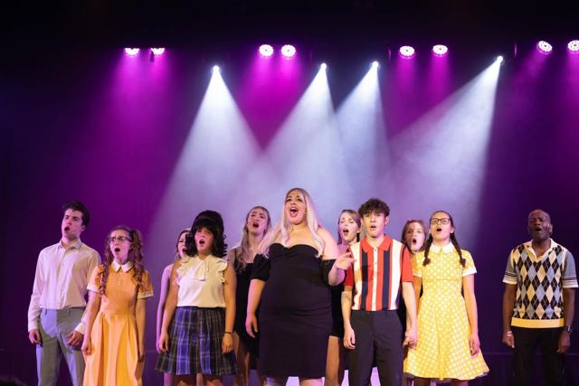 The cast lined up across the stage under spotlights
