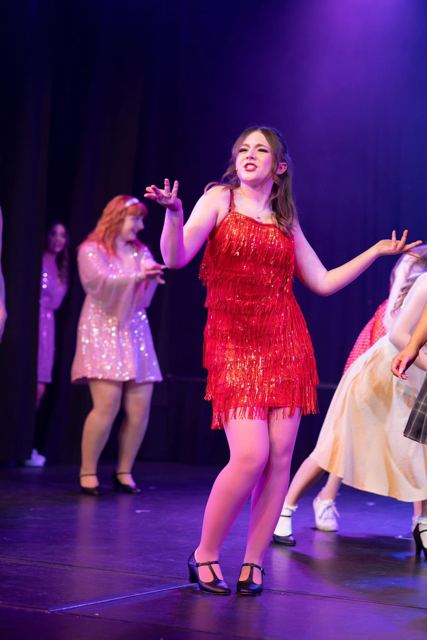 A performer in a red dress dancing under purple light