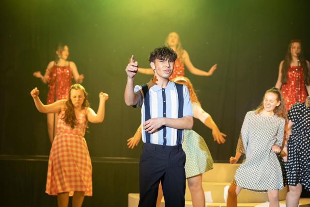 A dancer in a striped shirt leading the ensemble under yellow light