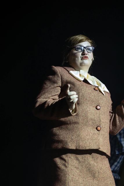 A performer in a tweed suit and glasses, pointing