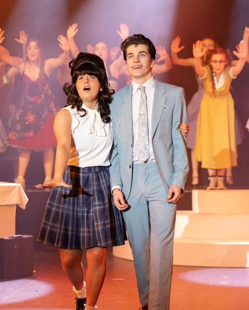 A performer in a beehive wig and a young man in a blue suit walking together
