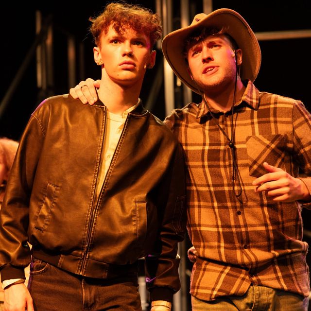 Two young men arm in arm, one in a cowboy hat