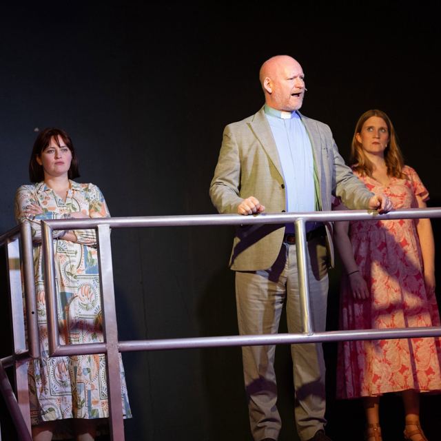 A man in a suit standing between two women at a rail