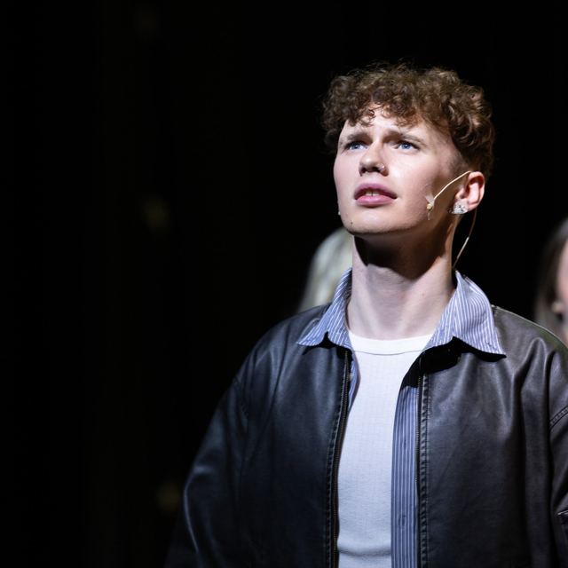 A young man in a leather jacket looking up into the light