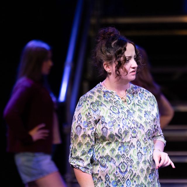 A woman in a patterned blouse on stage